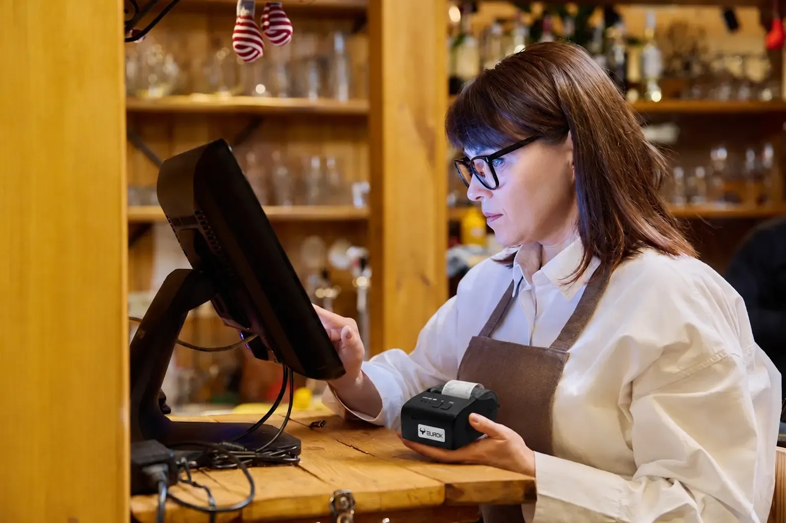 Server holding an AUROK portable thermal printer beside a restaurant POS screen